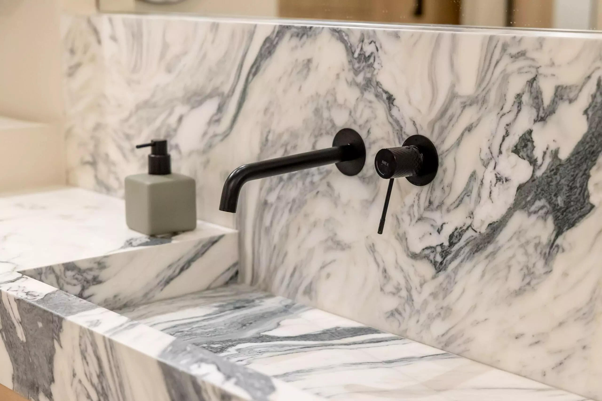 Lavemains élégant dans un vestiaire, avec un lavabo en marbre blanc et gris, et des griffoirs noirs pour un design sophistiqué et moderne