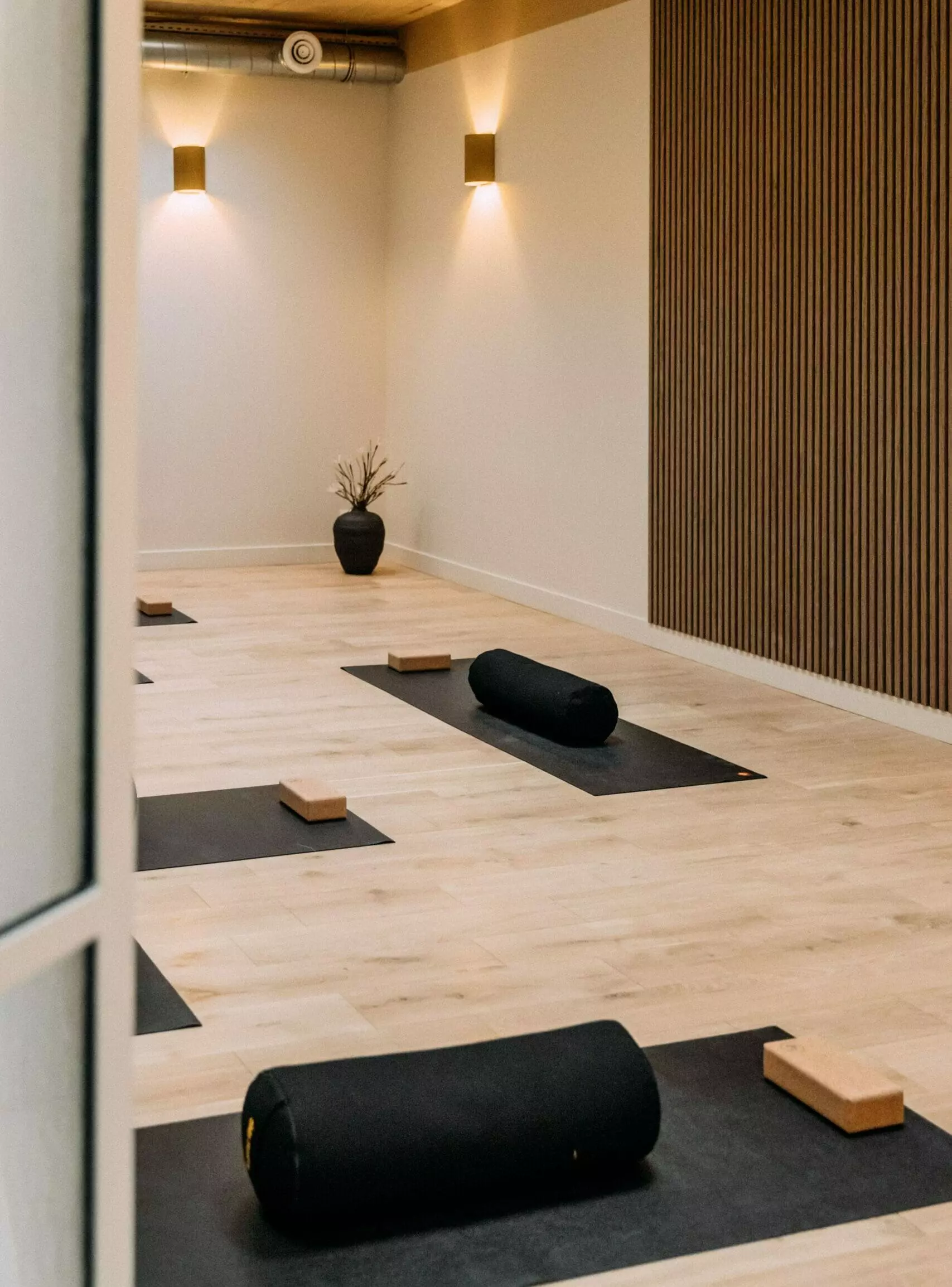 Salle de sport lumineuse avec parquet clair, murs blancs, miroirs, barres de danse et tapis de Pilates noirs soigneusement alignés dans une ambiance zen.