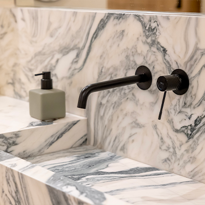 Lavemains élégant dans un vestiaire, avec un lavabo en marbre blanc et gris, et des griffoirs noirs pour un design sophistiqué et moderne