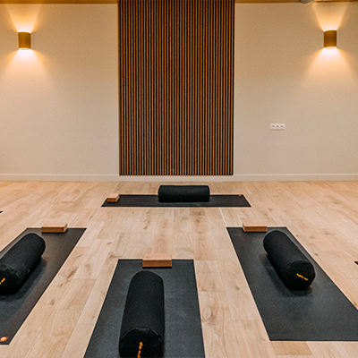 Salle de sport lumineuse avec parquet clair, murs blancs, miroirs, barres de danse et tapis de Pilates noirs soigneusement alignés dans une ambiance zen.