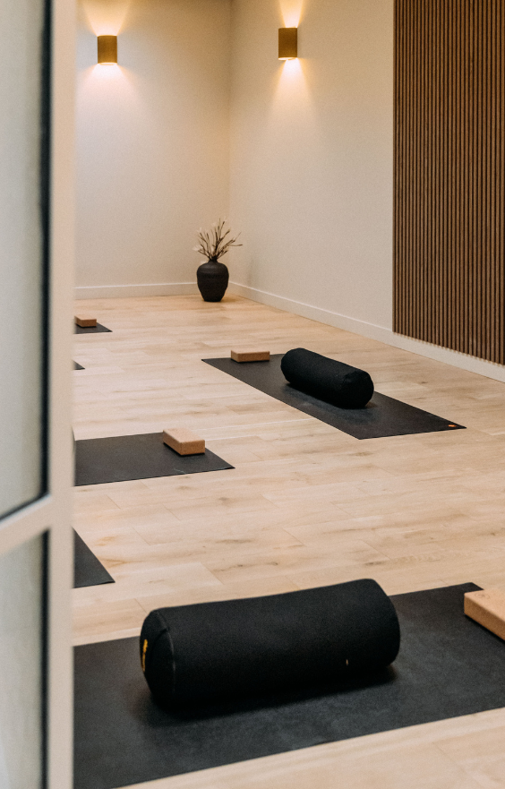 Salle de sport lumineuse avec parquet clair, murs blancs, miroirs, barres de danse et tapis de Pilates noirs soigneusement alignés dans une ambiance zen.