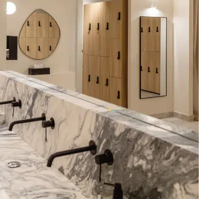 Lavemains élégant dans un vestiaire, avec un lavabo en marbre blanc et gris, et des griffoirs noirs pour un design sophistiqué et moderne