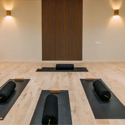 Salle de sport lumineuse avec parquet clair, murs blancs, miroirs, barres de danse et tapis de Pilates noirs soigneusement alignés dans une ambiance zen.
